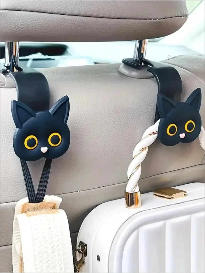 A set of two black cat headrest hooks with white yarn and gold accents attached to a light gray car seat.