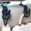 A set of two black cat headrest hooks with white yarn and gold accents attached to a light gray car seat.