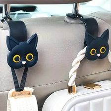 A set of two black cat headrest hooks with white yarn and gold accents attached to a light gray car seat.