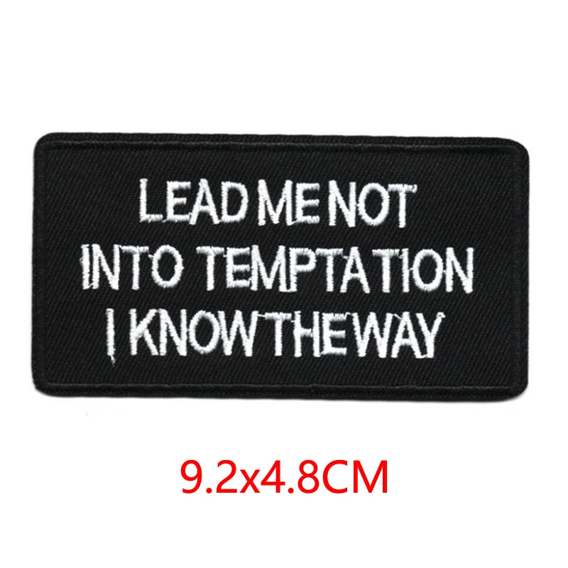 Black embroidered iron-on letter patch with white text that reads Lead me not into temptation I know the way