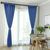 Blue fabric curtains hanging from a black rod in a bright room.