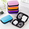 A stack of colorful silicone pouches and an open black pouch displaying white cables on a white laptop surface.