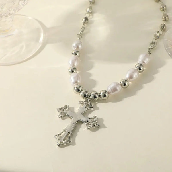 Collier argenté avec des perles blanches et un pendentif croix sur fond blanc.