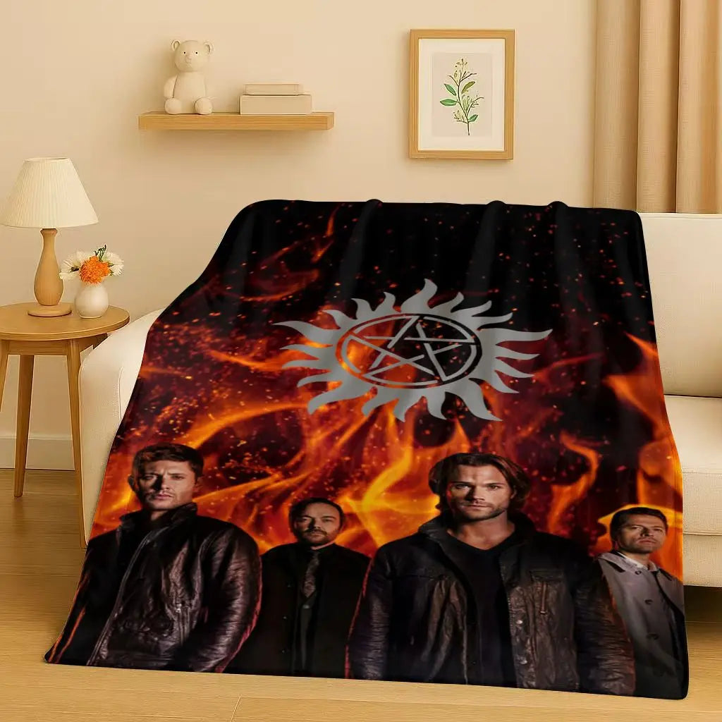 A dark blanket featuring a fiery sun emblem and portraits of characters from the Supernatural TV show
