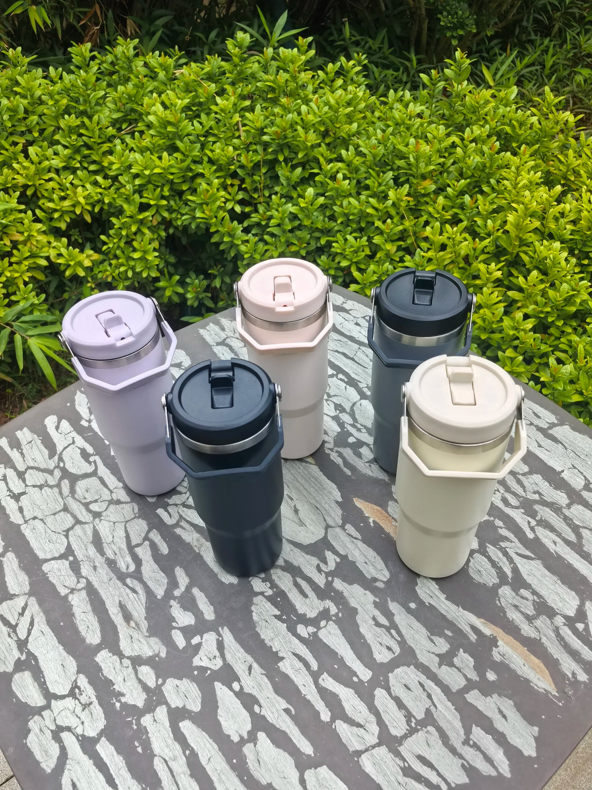 Four stainless steel vacuum insulated tumblers in various shades of gray and beige are displayed on a wooden surface.