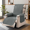 A gray quilted waterproof non-slip recliner sofa cover with side pockets resting on a floor.