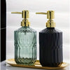 A pair of glass soap dispensers with gold pumps, one green and one dark blue, resting on a gold tray.