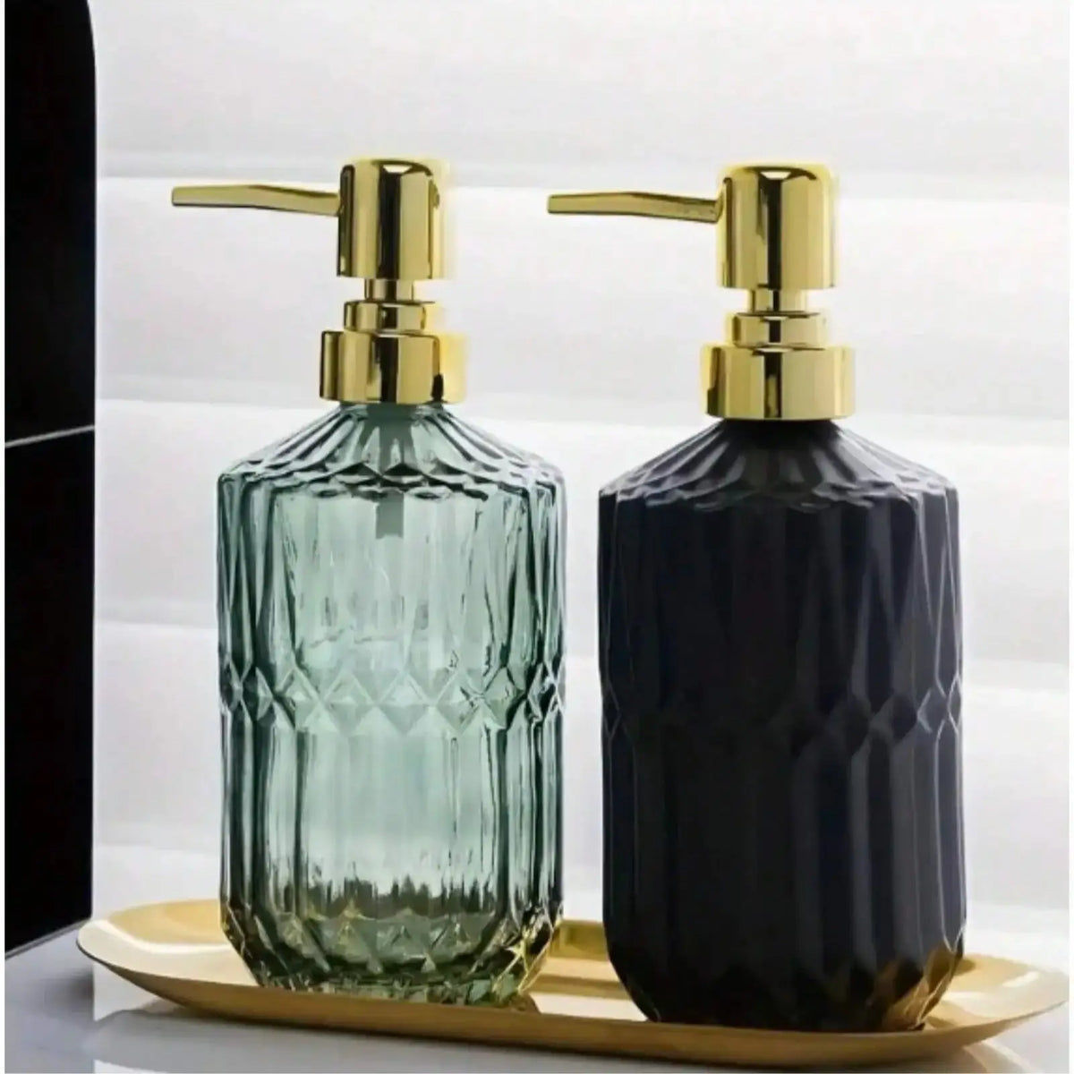 A pair of glass soap dispensers with gold pumps, one green and one dark blue, resting on a gold tray.