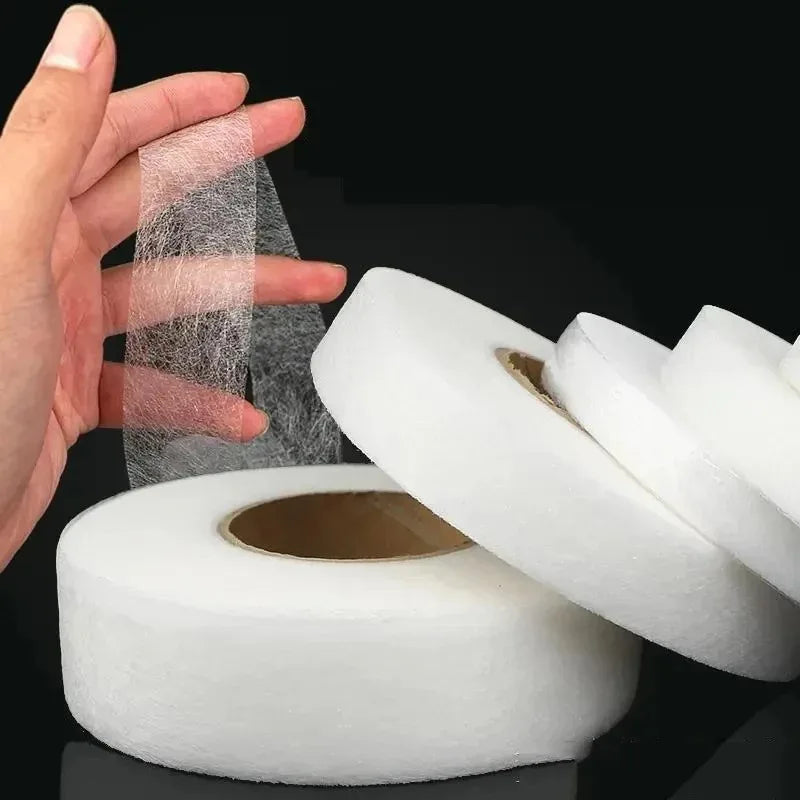 A hand holds a roll of double-sided iron-on adhesive tape for fabric hemming and repairs.
