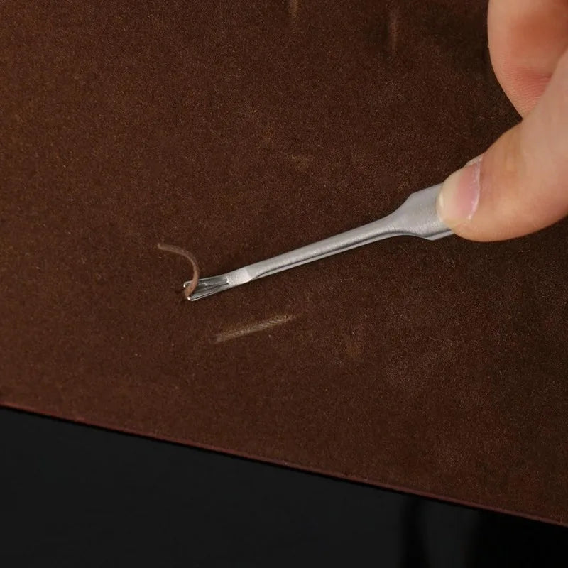 A hand holds a small metal leather edge groover and beveler tool against a brown leather surface.