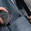 A hand is holding a foldable magnetic wireless charging stand for multiple devices against a gray fabric.