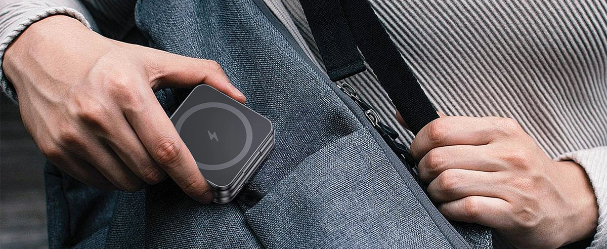 A hand is holding a foldable magnetic wireless charging stand for multiple devices against a gray fabric.