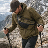 A man wearing a olive green jacket is hiking on rocky terrain while carrying an everyday nylon crossbody bag.