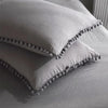 A white duvet cover set with a soft, textured fabric and decorative pom-pom trim is folded on a bed.