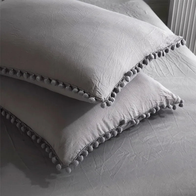 A white duvet cover set with a soft, textured fabric and decorative pom-pom trim is folded on a bed.