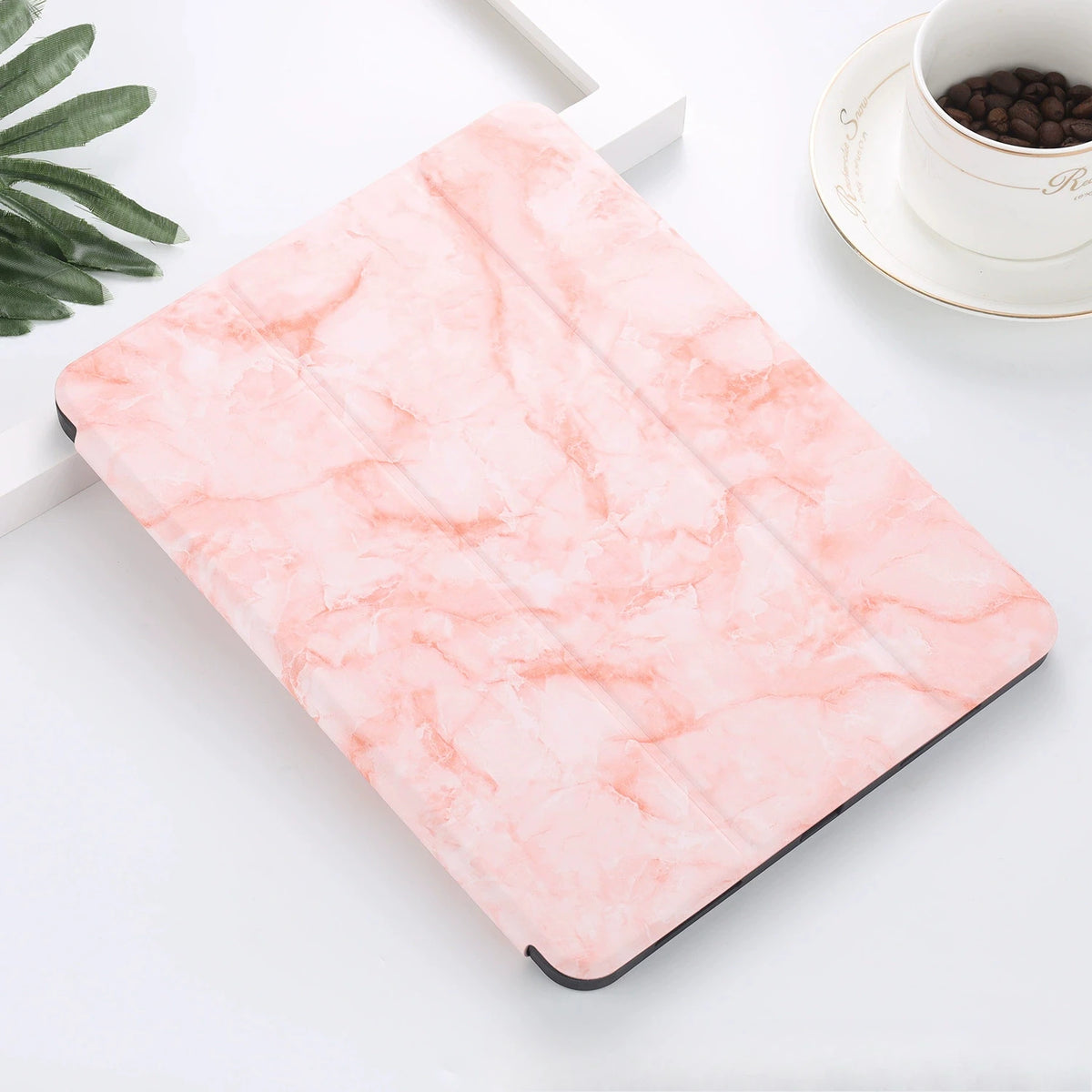 A pink marble patterned case for an iPad Pro with a built-in pencil holder resting on a white surface.