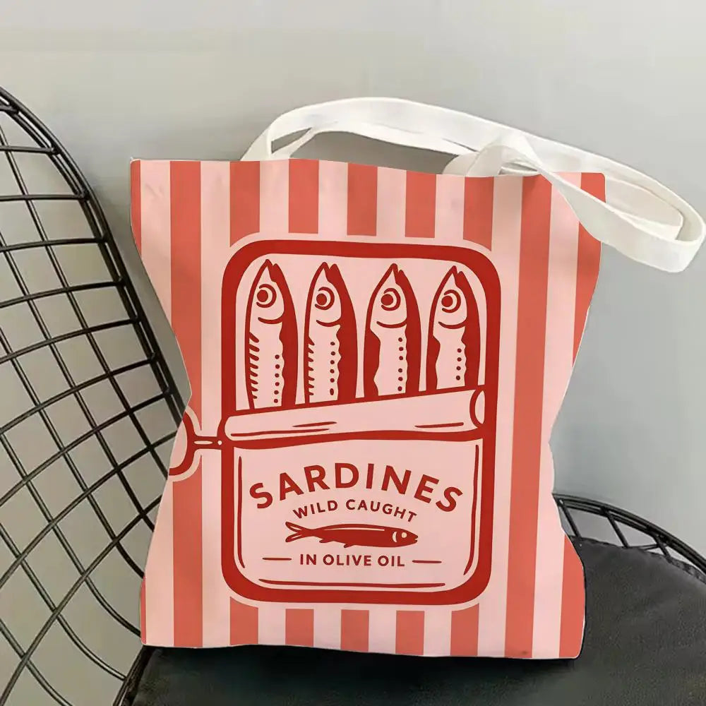 A pink and white striped canvas tote bag featuring a graphic print of sardines in olive oil.