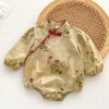 A light beige floral lace cotton romper for a baby girl lying on a woven mat.