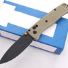A compact folding knife with a light tan handle and black blade is shown resting on a blue box.