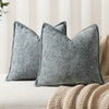 Two gray chenille throw pillows resting on a beige sofa with a knitted throw blanket.