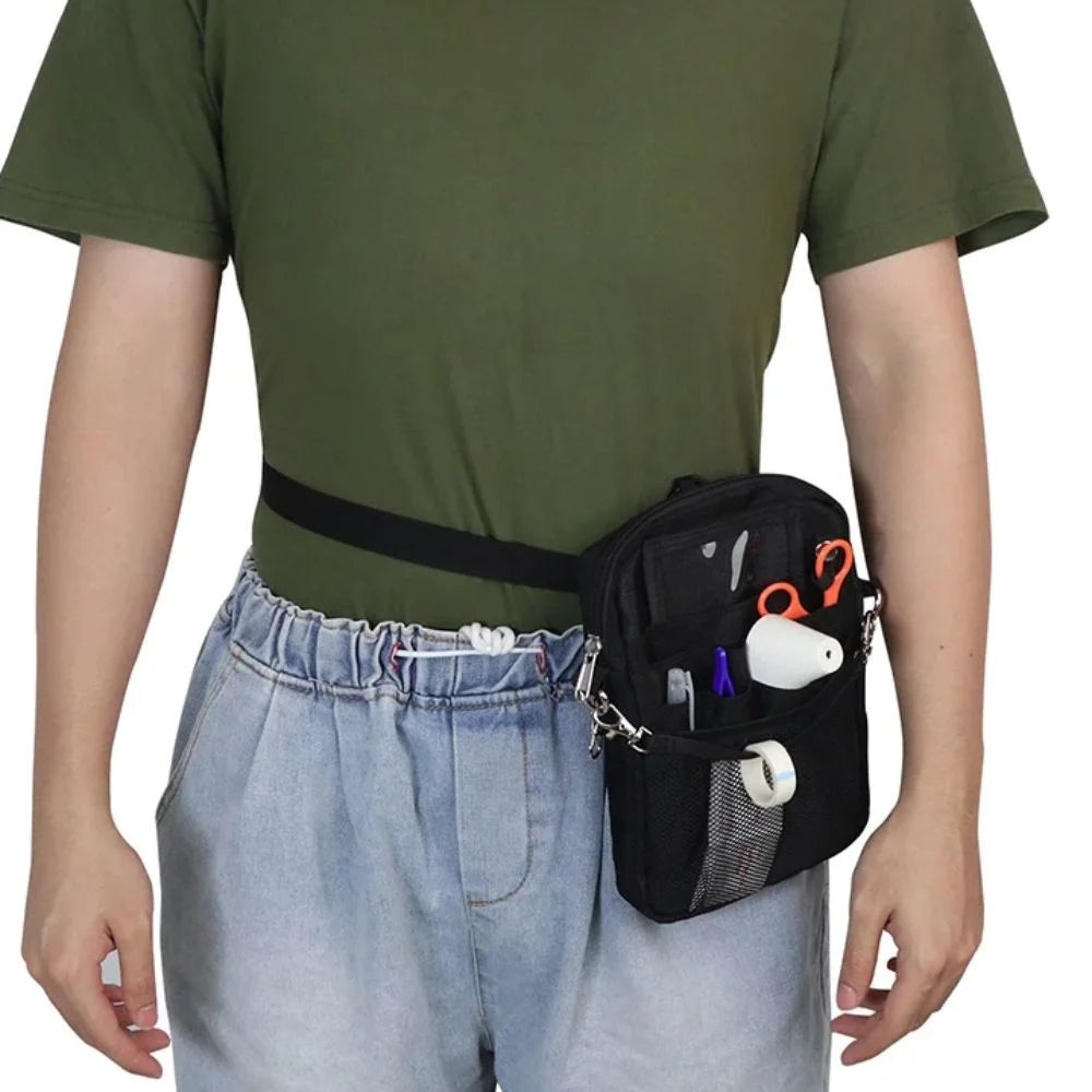 A person wearing a dark green t-shirt and light blue jeans is holding a black multi-pocket crossbody fanny pack.