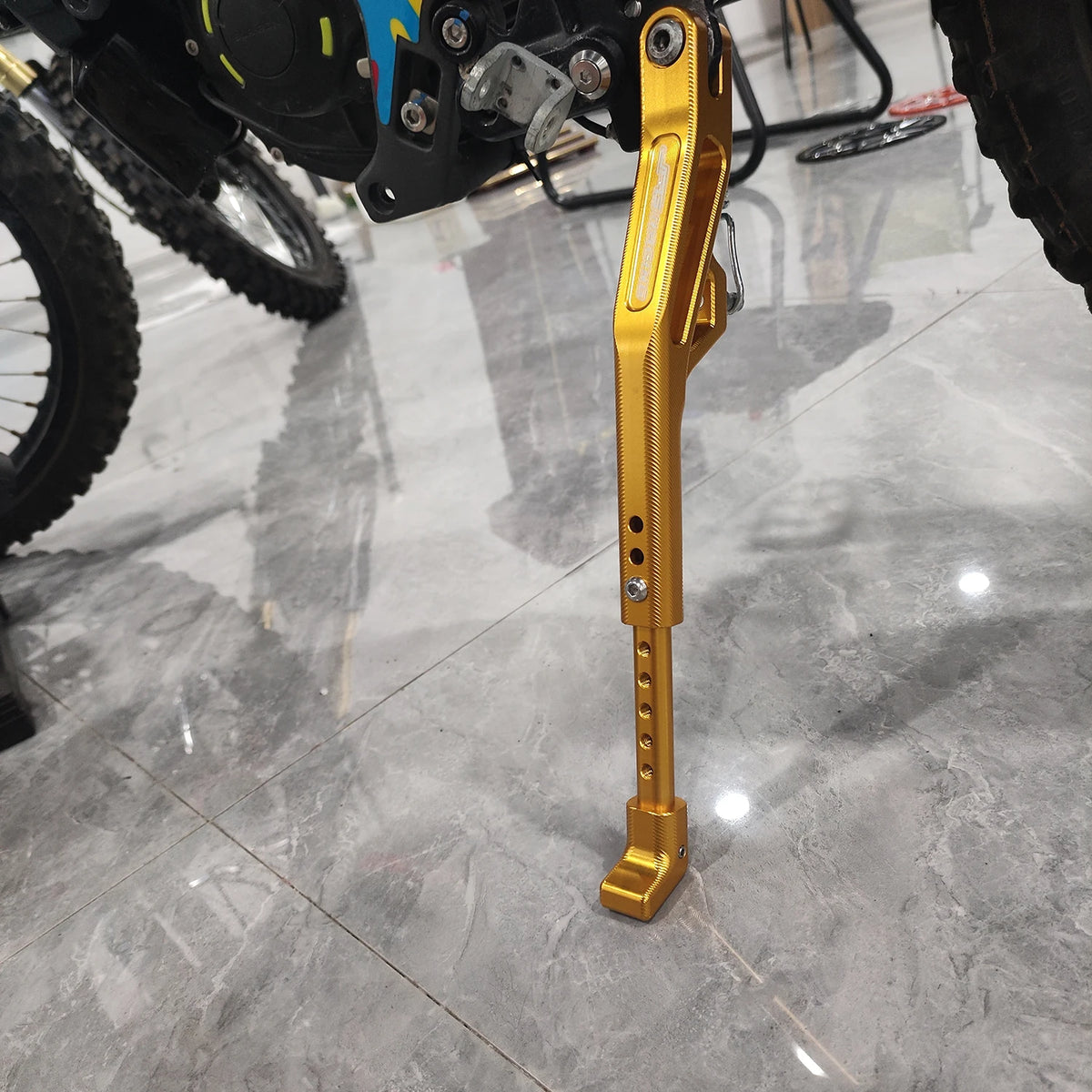 Close-up of a gold-colored CNC aluminum adjustable motorcycle kickstand for Sur Ron and Segway.