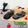 A black and gray RC drift stunt car is displayed on a tan cloth with several red traffic cones.