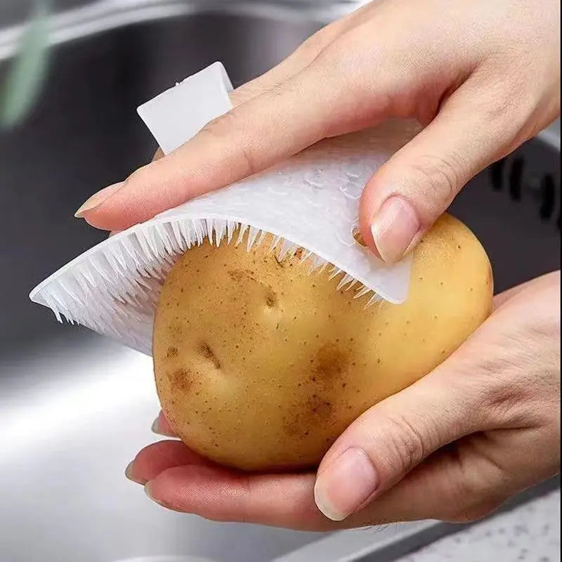 Une main tient une pomme de terre jaune avec un écume silicone et un brosse à fissures attachés.