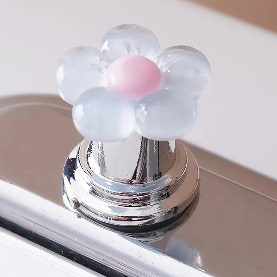 A floral toilet flush handle featuring translucent white and pink ceramic flowers, resting on a chrome fixture.