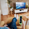 A hand holds a lime green silicone remote control cover for a TV, resting on a couch.