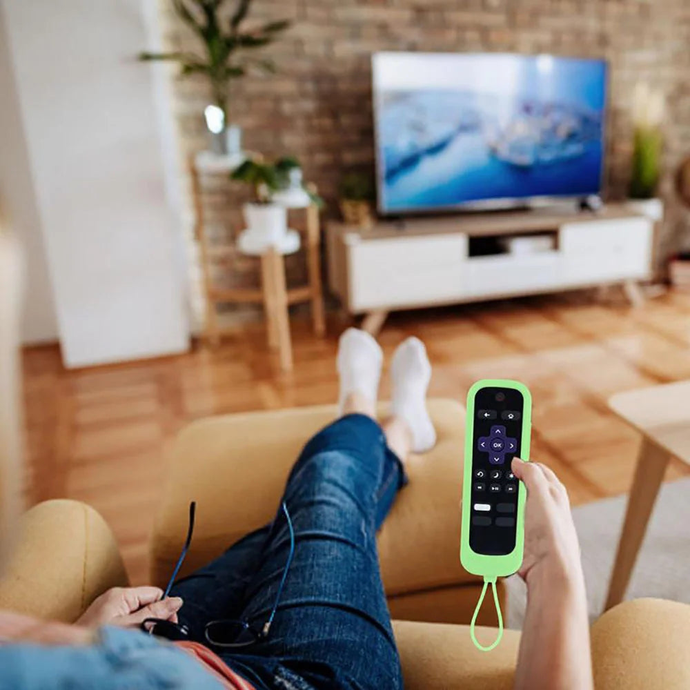 A hand holds a lime green silicone remote control cover for a TV, resting on a couch.