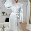 A white silk satin robe with lace trim is displayed on a mannequin in an indoor setting.