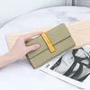 A beige women's cowhide leather bifold wallet with a yellow strap is shown resting on a light wooden board next to a magazine