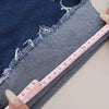 A hand measures the length of dark blue denim fabric using a ruler.