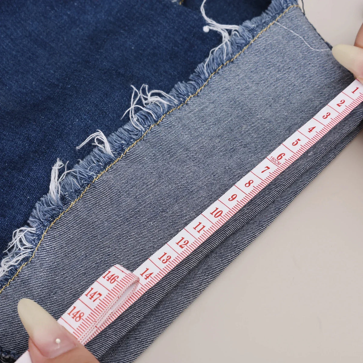 A hand measures the length of dark blue denim fabric using a ruler.