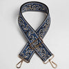 A dark blue and white paisley jacquard bag strap with gold-toned hardware, shown crossed.