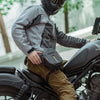 A person wearing a black helmet and gray jacket is sitting on a motorcycle with a black hip pack.