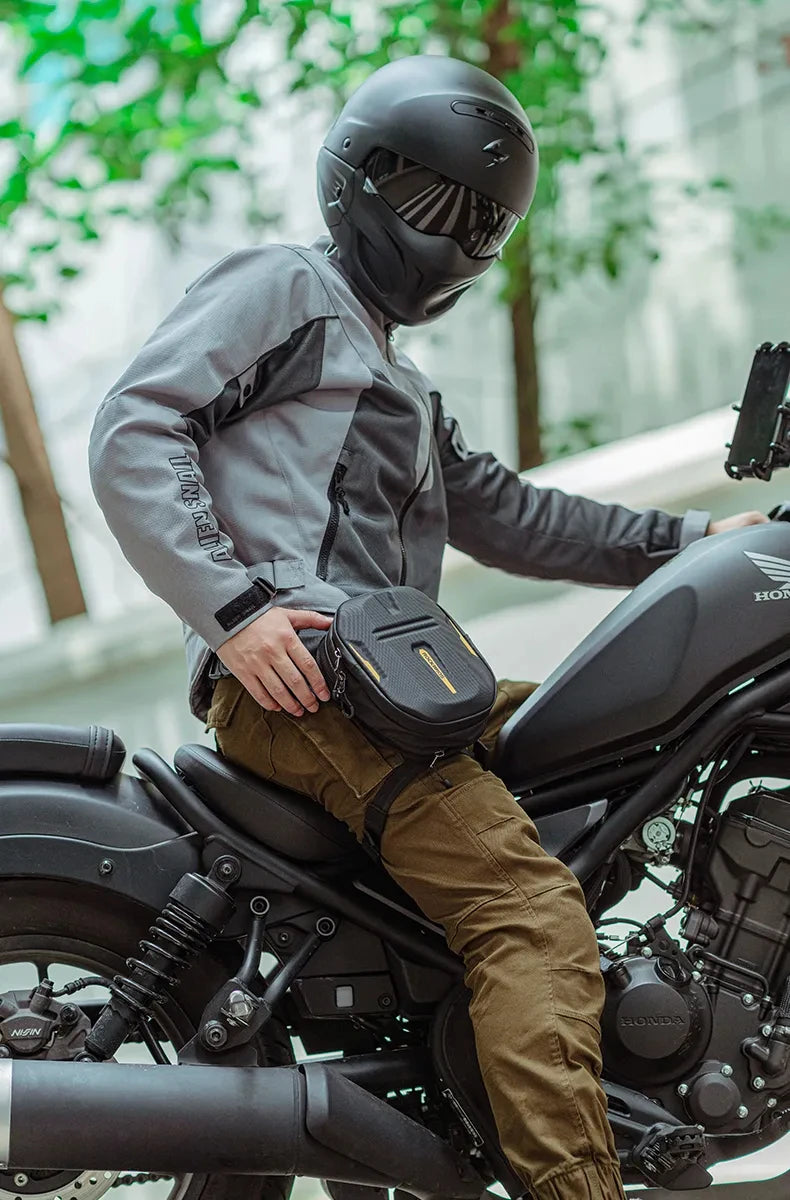 A person wearing a black helmet and gray jacket is sitting on a motorcycle with a black hip pack.