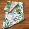 A folded pure cotton embroidered cartoon face towel featuring green and white floral patterns.