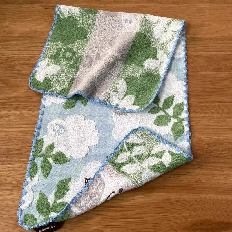 A folded pure cotton embroidered cartoon face towel featuring green and white floral patterns.