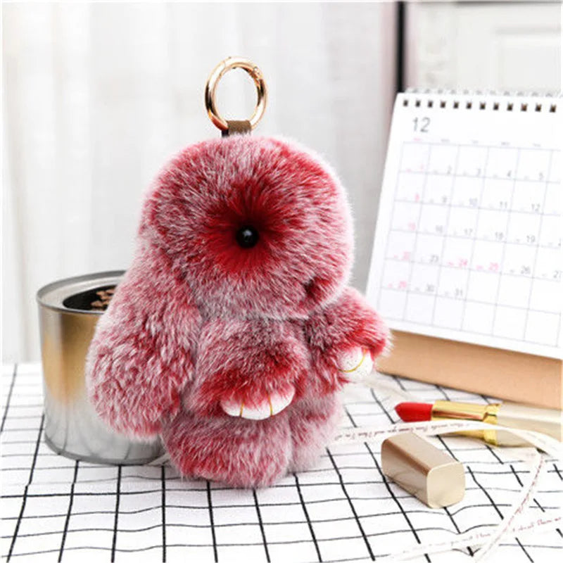 A fluffy red bunny keychain with a pom pom tail resting on a checkered surface.