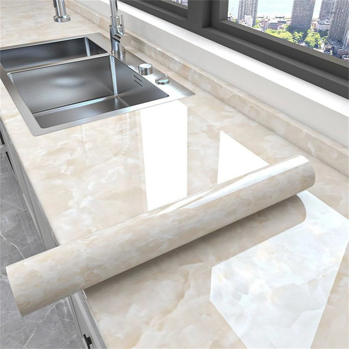 A stainless steel kitchen sink and a rolled-up piece of glossy beige marble-patterned vinyl wallpaper on a countertop.