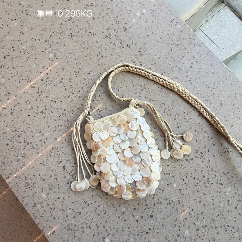 A light beige sequin accent chain shoulder bag resting on a speckled surface.