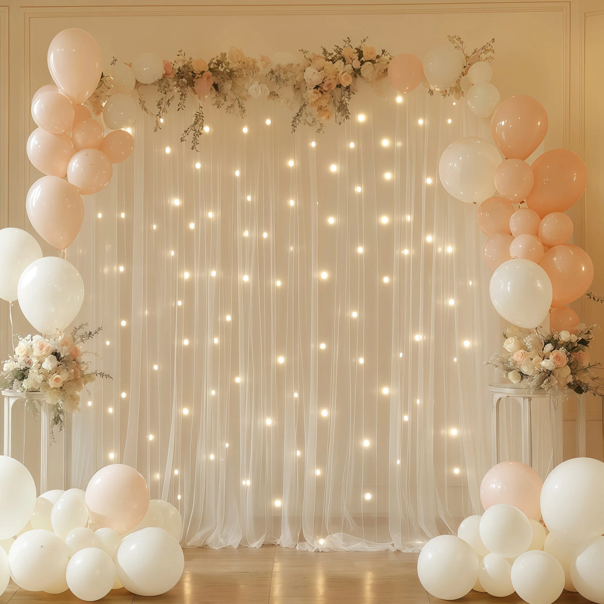 A backdrop setup featuring sheer tulle curtains decorated with warm white string lights and clusters of pink and white balloo