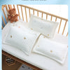 A display of soft breathable baby pillows with quilted white covers and small embroidered stars on a wooden crib railing.