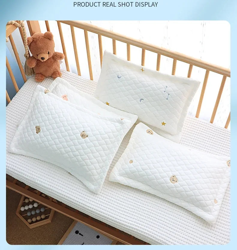 A display of soft breathable baby pillows with quilted white covers and small embroidered stars on a wooden crib railing.