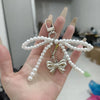 A hand holds a pearl beaded bow keychain with a heart charm.