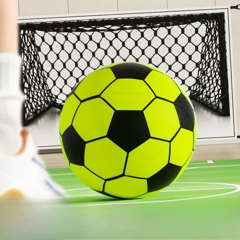 A bright yellow and black soccer ball is positioned in front of a black mesh goal net on a green surface.