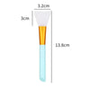 A silicone facial mask brush with a white head, gold ferrule, and light blue handle.