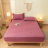 A pink fitted bed sheet set with matching pillowcases is displayed on a wooden bed frame in a bright bedroom.
